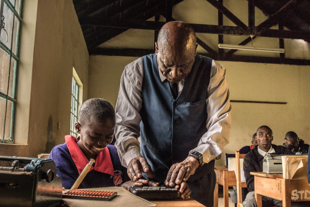 An older male teacher is helping a young student with the Orbit Reader